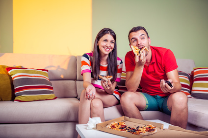 Funky young couple eating pizza on a couch in front of a green wall